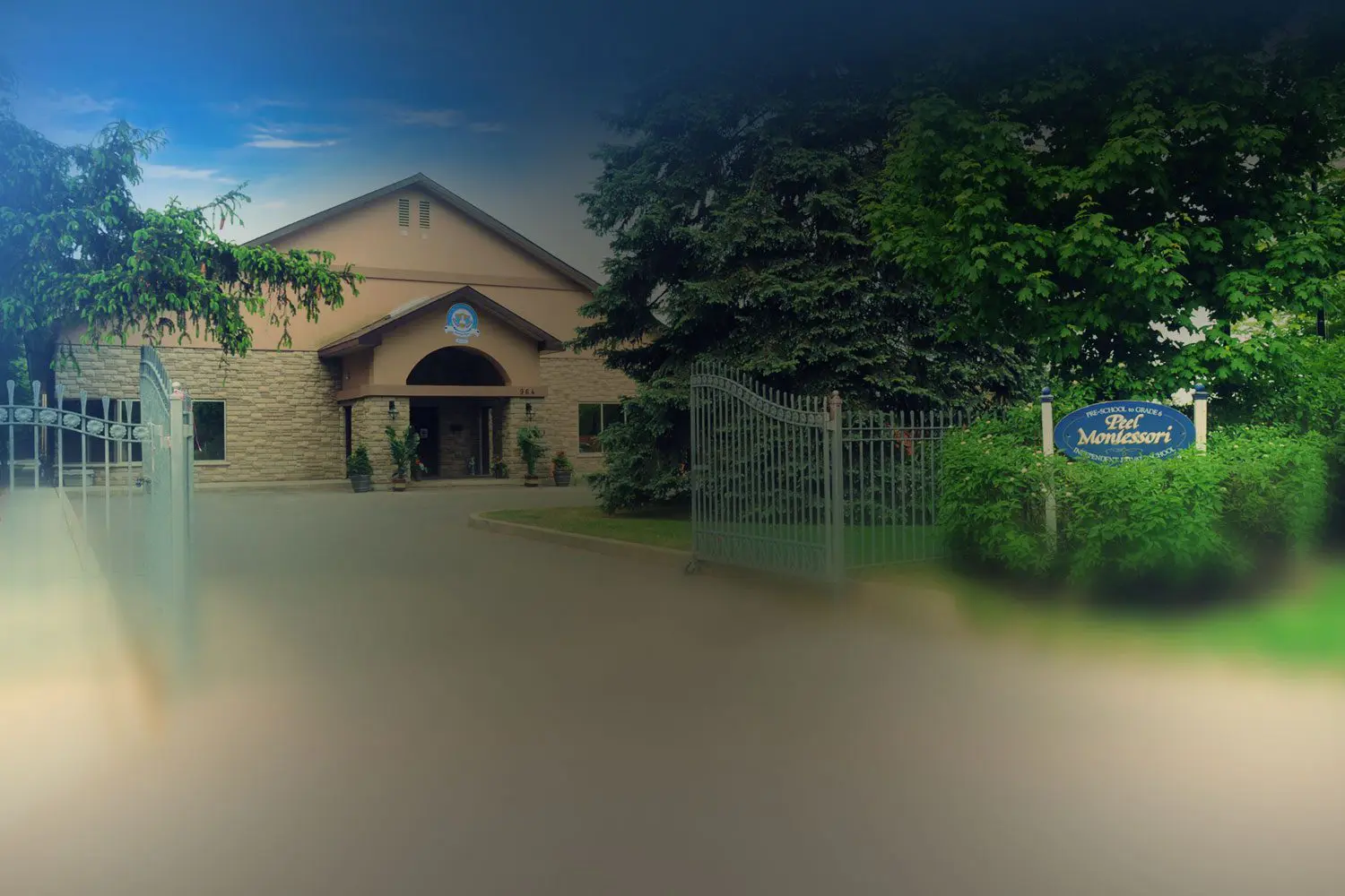 Entrance gate of a Montessori school with a blue and yellow sign. The building has a peaked roof, surrounded by trees and greenery.