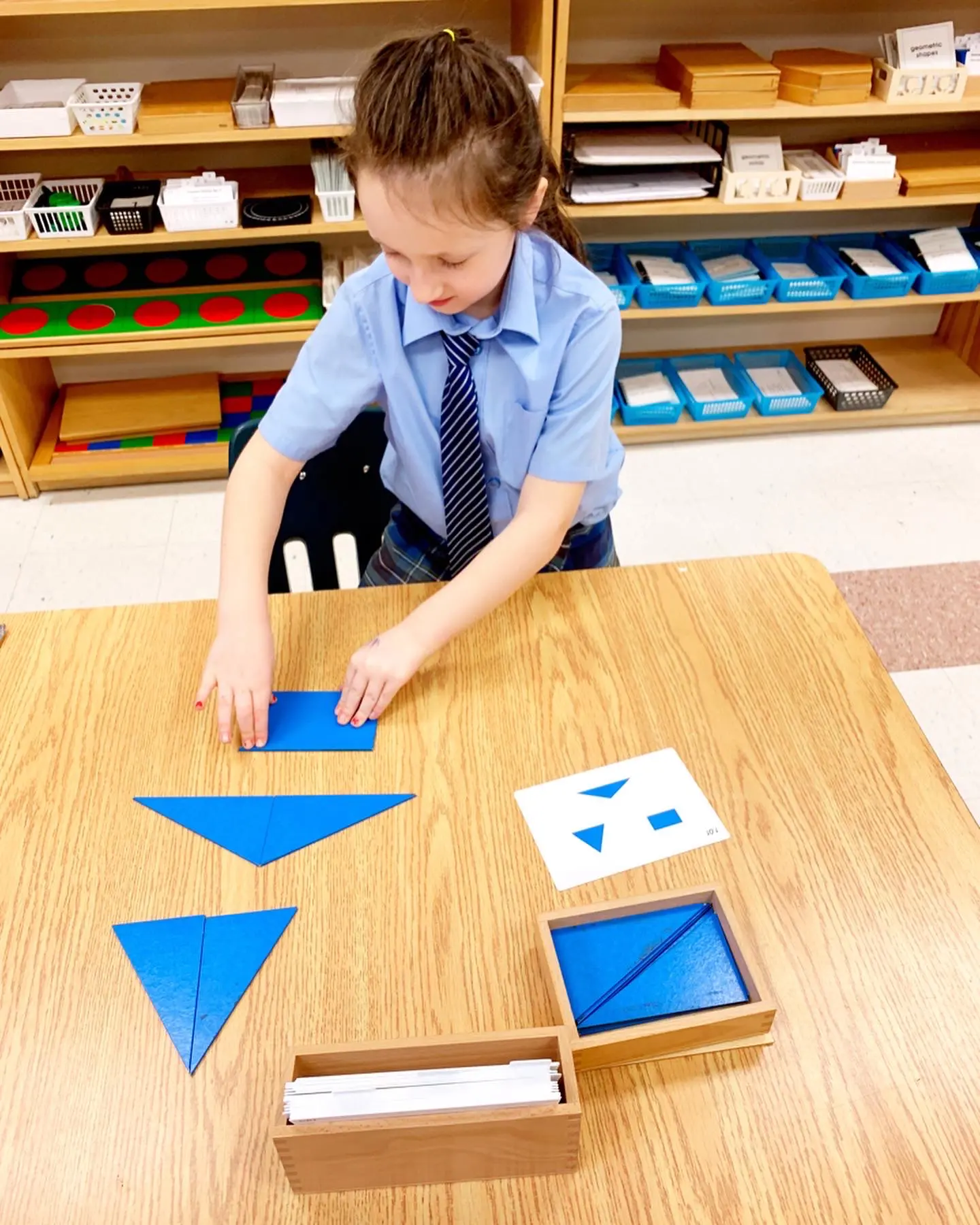 Child arranging blue geometric shapes on table.