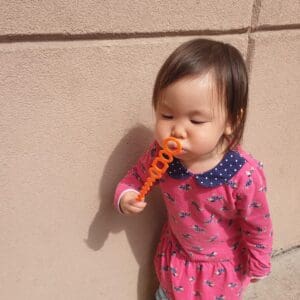 Toddler playing with an orange bubble wand.