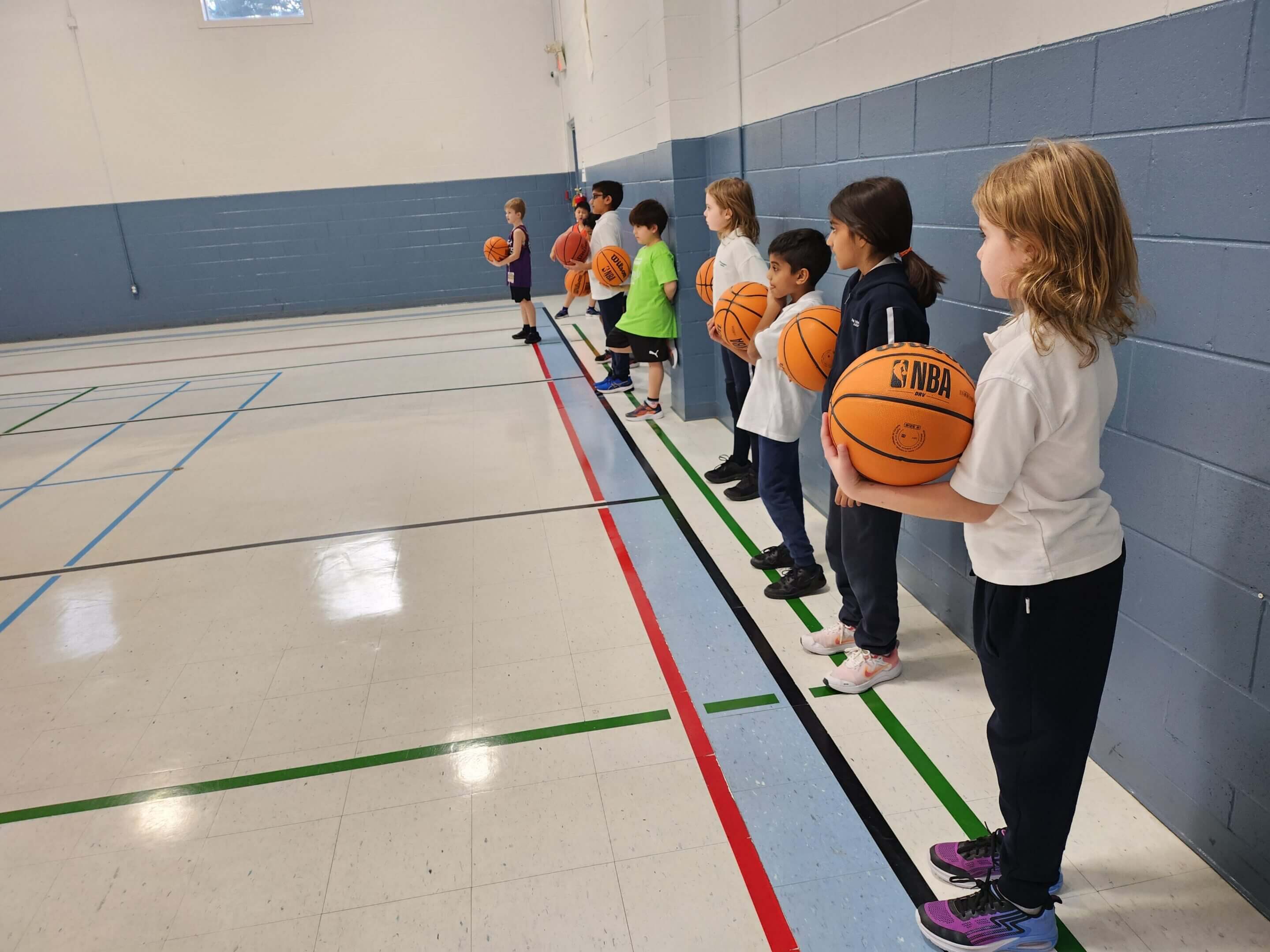 Children holding basketballs in a gym.