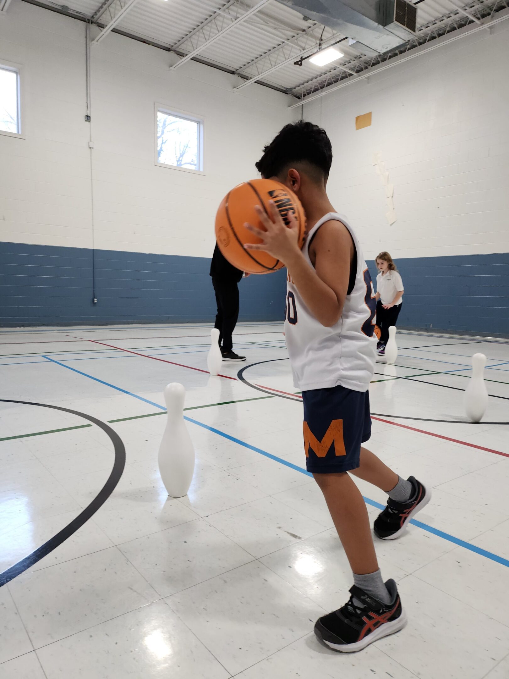 Child playing basketball in gymnasium setting.