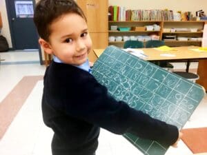 Smiling child holding a chalkboard in class.