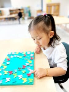 Child arranging colorful paper shapes on table.