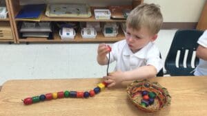 Child threading colorful beads on a string.