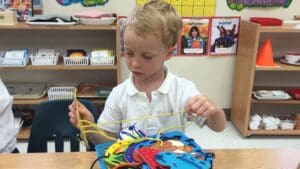 Child threading colorful shapes with a string.