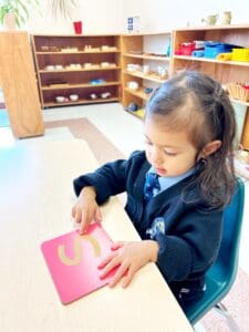 Child tracing letter "S" on pink card.