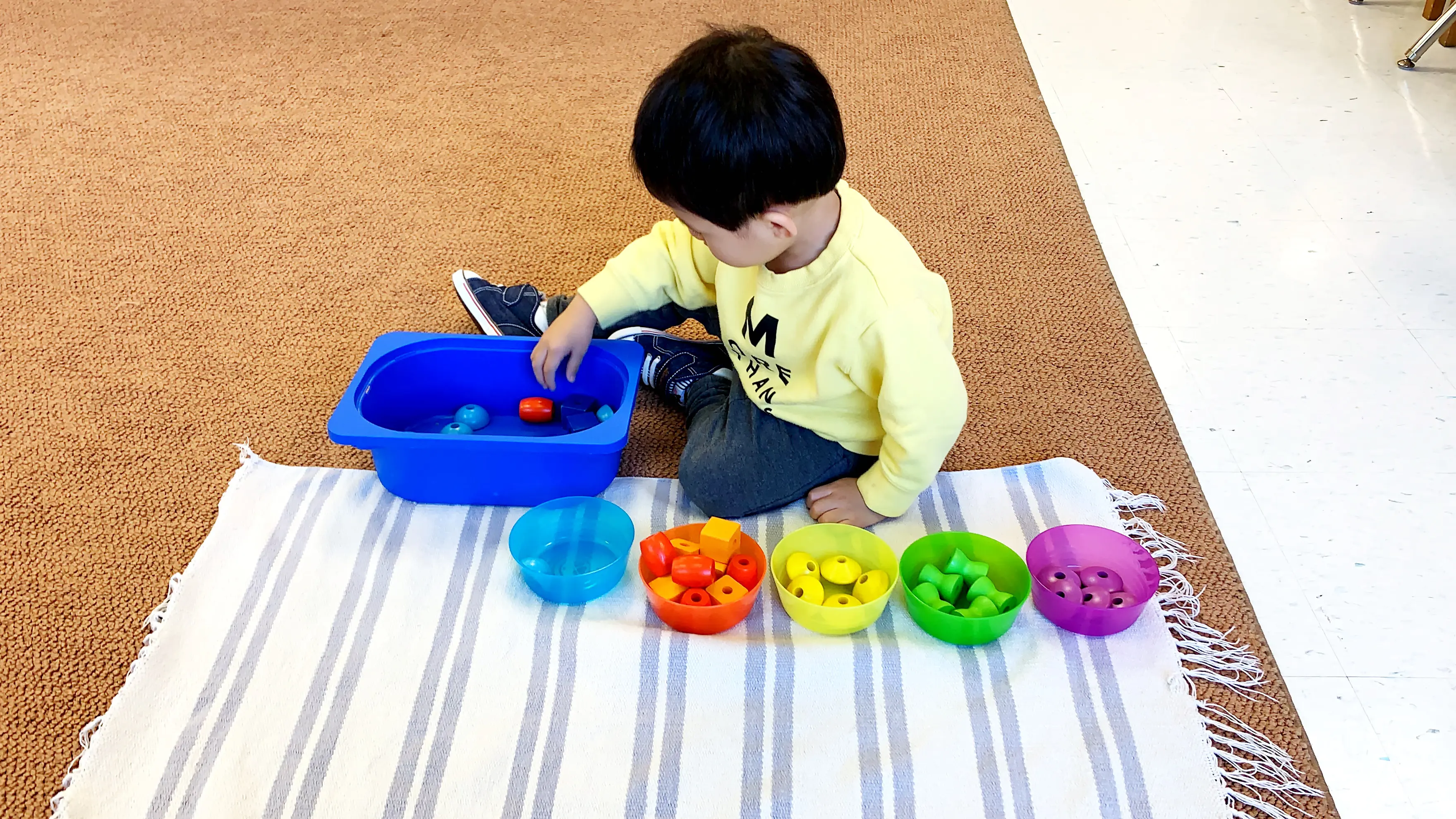 Child sorting colorful toys in blue container.