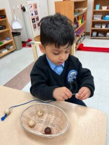 Child threading beads in a classroom setting.